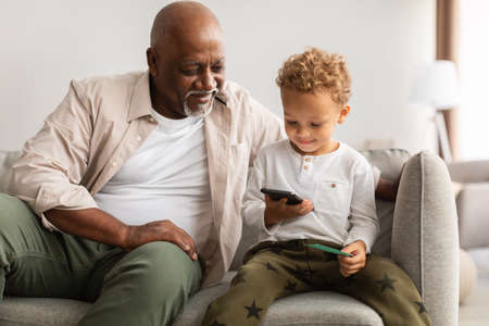 Black Grandfather And Little Grandson Using Cellphone Together At Home