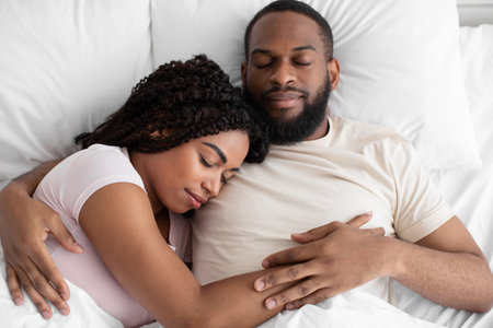 Calm young african american guy and woman sleeping, hugging on white bed in bedroom, top viewの写真素材