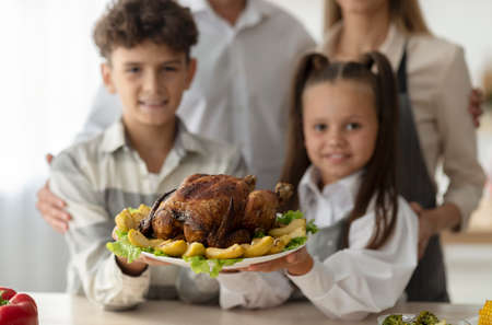 Happy children and parents holding roasted turkey served with apples on plate for Christmas dinner, selective focusの写真素材