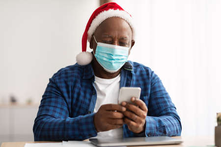 Black Male In Santa Hat And Mask Using Phone Indoor