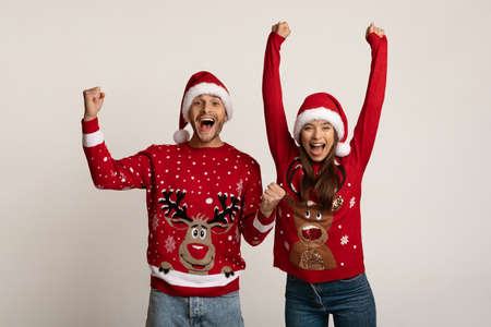 Hooray. Overjoyed Couple In Xmas Sweaters Celebrating Success With Raised Fistsの写真素材