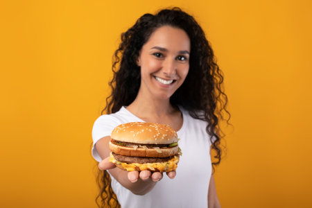 Happy Young Lady Holding And Giving Burger At Studioの写真素材