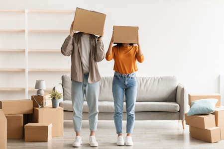 Silly young couple stading with carton boxes on their heads in new apartment on moving day, copy spaceの写真素材