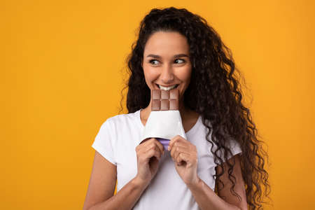 Funny Latin Lady Holding And Biting Chocolate At Studioの写真素材