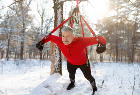 Athletic senior man doing bungee fitness exercises, training outdoors on sunny winter morningの写真素材