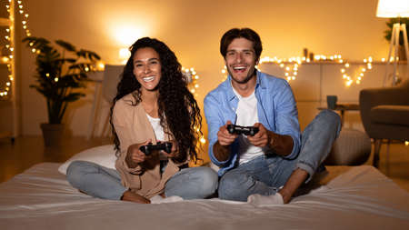 Young Husband And Wife Playing Videogame Sitting In Bedroom, Panorama