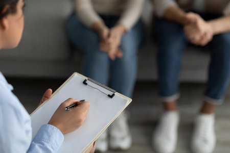 Marital counselor taking notes at therapy session with young spouses, holding clipboard and filling information formの写真素材