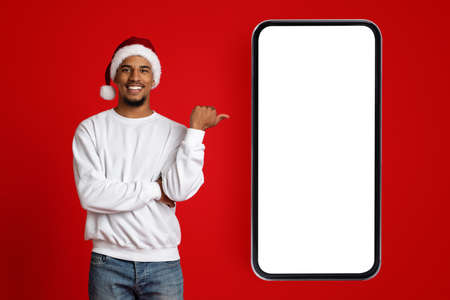 Positive black guy In Santa hat pointing at smartphone, mockupの写真素材