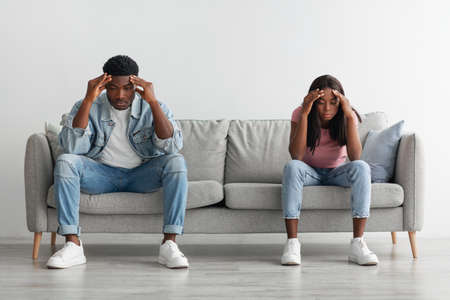 Depressed young black couple sitting on couch and thinkingの写真素材