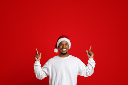 Charismatic african american guy in Santa hat pointing upの写真素材