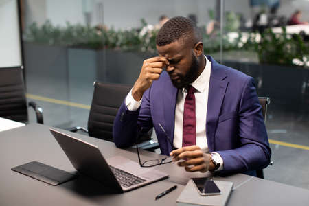 Exhausted african american businessman working on laptop at officeの写真素材