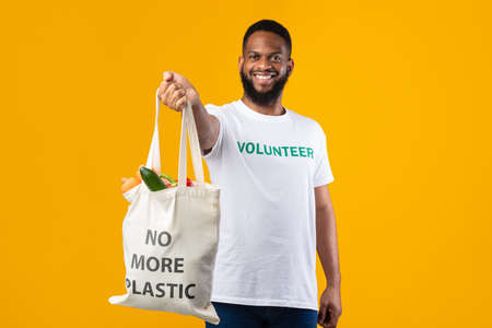 African American Volunteer Guy Showing White Shopper Bag, Yellow Backgroundの写真素材
