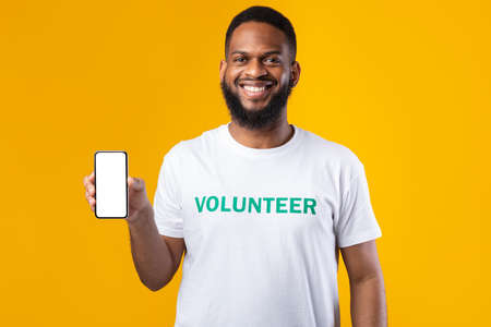 African Volunteer Man Shows Blank Smartphone Screen, Yellow Background, Mockupの写真素材