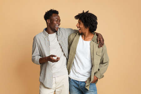 Two Cheerful Black Male Friends Embracing And Laughing On Beige Backgroundの写真素材