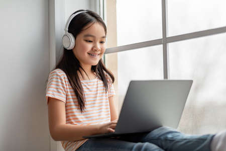 Closeup of cheerful asian girl with wireless headset using laptopの写真素材