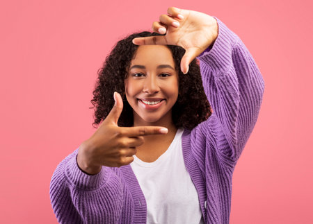 Cheerful black woman making picture frame with fingers, looking at camera and smiling for photo on...