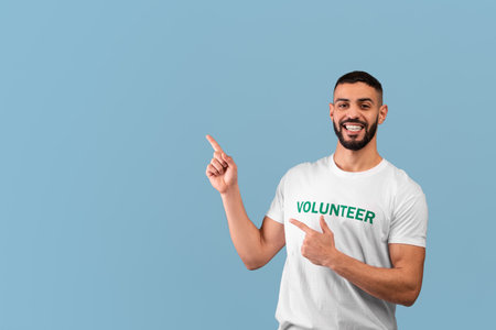 Middle eastern male volunteer pointing fingers aside at empty space for your text or ad, posing over blue backgroundの写真素材