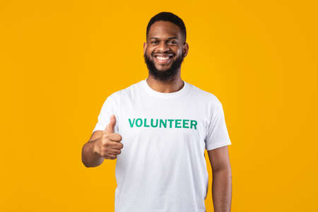 Happy African American Male Volunteer Gesturing Thumbs-Up Over Yellow Backgroundの写真素材