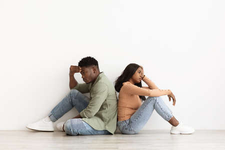 Upset african american couple sitting back to back on floorの写真素材