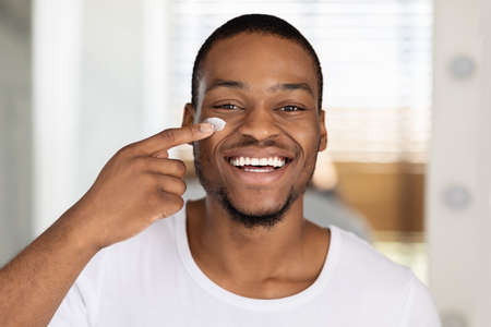 Closeup Shot Of Smiling Handsome Black Man Applying Moisturising Cream On Faceの写真素材