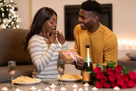 Black Boyfriend Surprising Girlfriend With Wrapped Gift Celebrating Valentine Indoorの写真素材