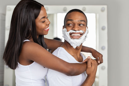 Cheerful Black Couple Embracing In Bathroom While Making Beauty Routine At Homeの写真素材