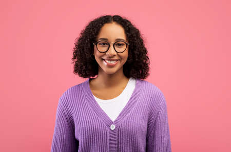 Happy young African American woman with beautiful smile and curly hair looking at camera, posing...