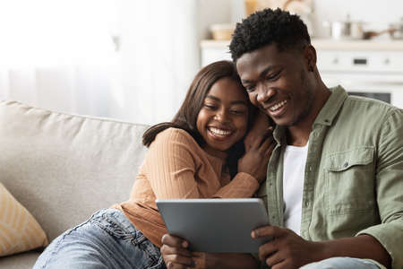 Happy black lovers using digital tablet together, home interiorの写真素材