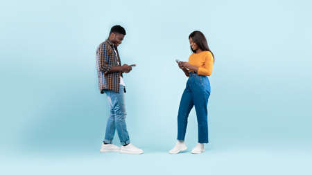 African american couple using cellphones, blue studio wallの写真素材
