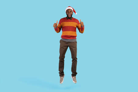 Holiday Offer. Black Man In Santa Hat Jumping And Gesturing Thumbs Up