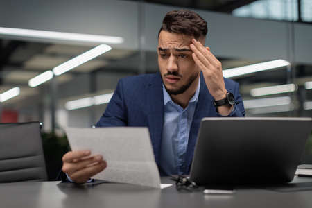Puzzled middle eastern manager reading financial report, copy space