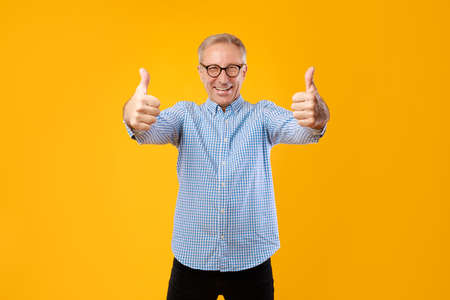 Happy mature guy gesturing thumbs up and smiling at studio