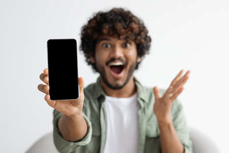 Modern smartphone with blank screen in excited indian guy hand