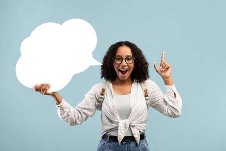 Happy black woman holding blank speech bubble, having creative idea on blue studio background,...