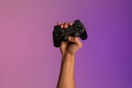Unrecognizable young man holding video game joystick in neon light, closeup of handの写真素材
