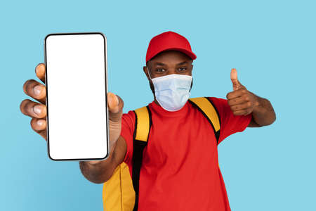 Safe Food Delivery. Black Courier Man Wearing Medical Mask Showing Blank Smartphone