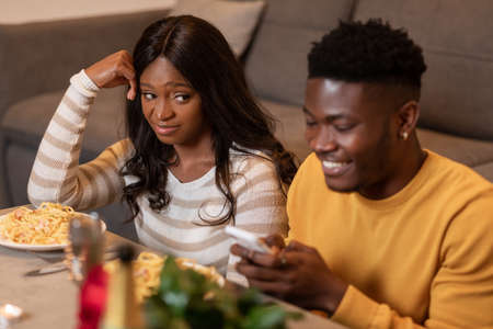 Displeased Girlfriend Looking At Boyfriend Using Smartphone During Date Indoor