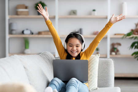 Emotional asian girl with wireless headset using laptop at home