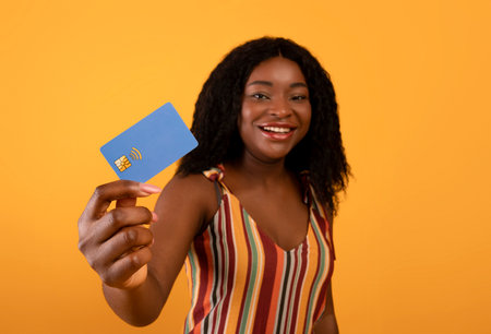 Beautiful black woman showing credit card on orange background, selective focus. Contactless...
