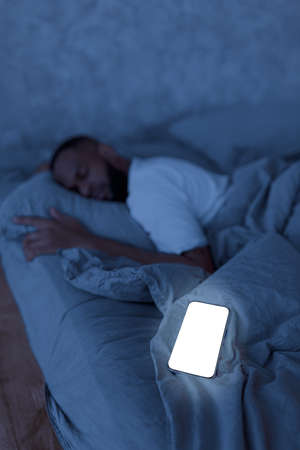Young African American man sleeping in bed with cellphone