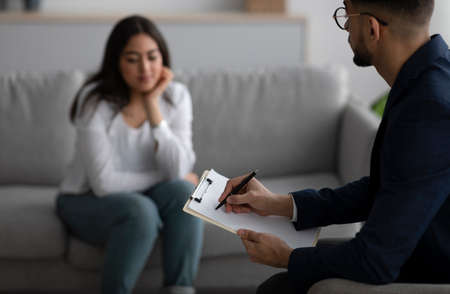 Psychological therapy. Male psychologist noting problems of young arab woman at psychotherapy session, selective focusの写真素材