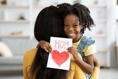 Cute Little Black Girl Holding Handmade Greeting Card And Embracing Momの写真素材