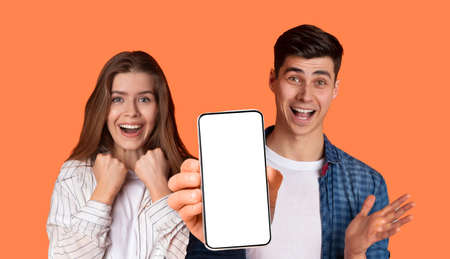 Happy young couple showing mobile phone with empty screen, mockupの写真素材