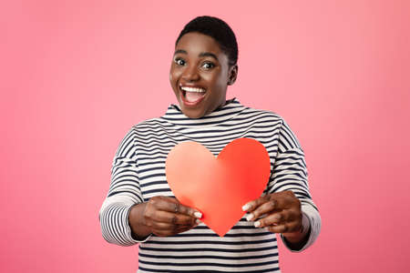 Cheerful Overweight Black Lady Showing Red Paper Heart, Pink Backgroundの写真素材