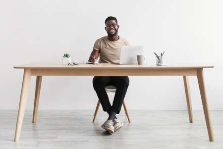 Smiling African American man writing in notebook, taking notes and using computer, sitting at desk in home office, copy spaceの写真素材