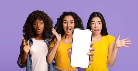 Amazed multiethnic ladies showing smartphone with blank screen