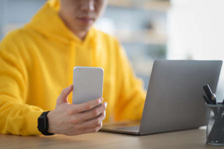 Asian man sitting at desk using cell phone
