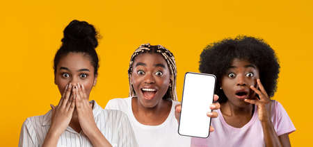Amazed black women showing smartphone with empty screen, mockupの写真素材