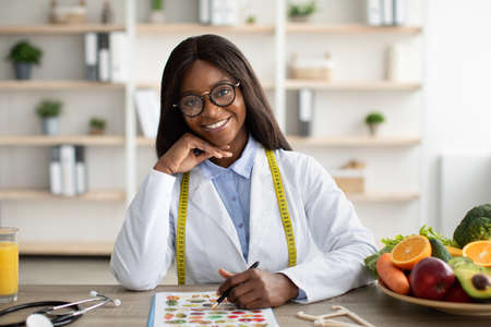Portrait of happy african american weight loss consultant sitting at workplace and smiling at camera in modern clinicの写真素材