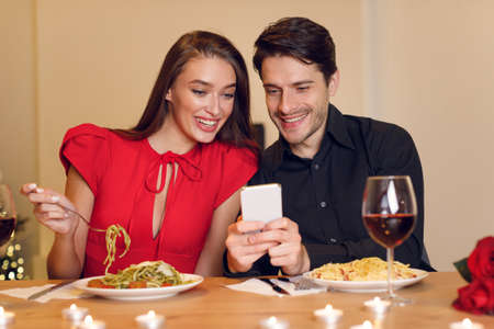 Smiling man and woman using mobile phone during dinnerの写真素材